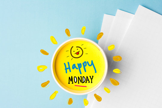An image with a blue background, some white paper on the right side of the image, and a coffee cup that has some yellow liquid in it and that words happy Monday. There is a smiley face drawn inside the cup as well.
