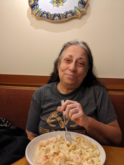 A photo of my mother-in-law sitting at a restaurant eating pasta. 