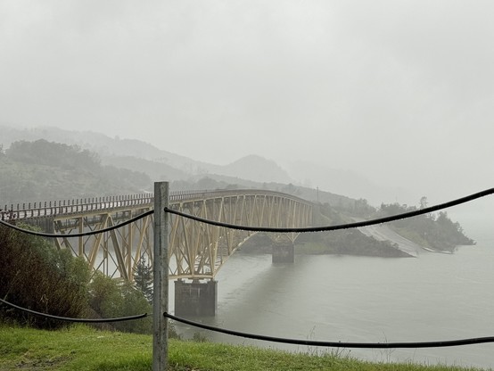 Long bridge over a body of water to a fog-soaked hill. 