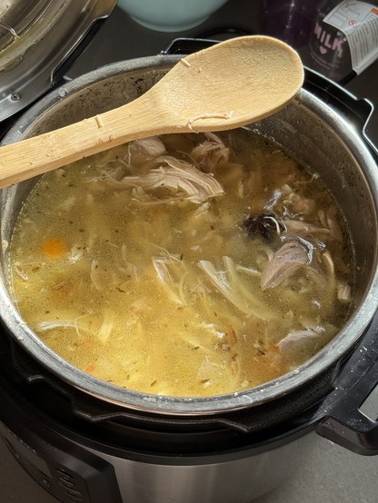 A pot of chicken soup with a wooden spoon laying across the top. 