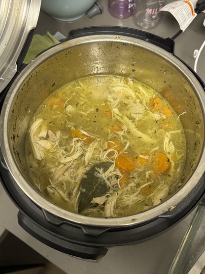 Top-down shot of an instant pot filled with a broth loaded with carrots and shredded chicken 