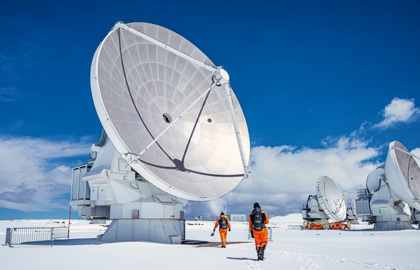 Some ALMA antennas at the Chajnantor plateau with partially cloudy skies and a bit of snow. Two ALMA workers wearing high-visibility orange suits and backpacks with oxygen tanks can be seen walking in the direction to the foremost antenna.

Image by our colleague Pablo Bello (IG: @pablitocl).
