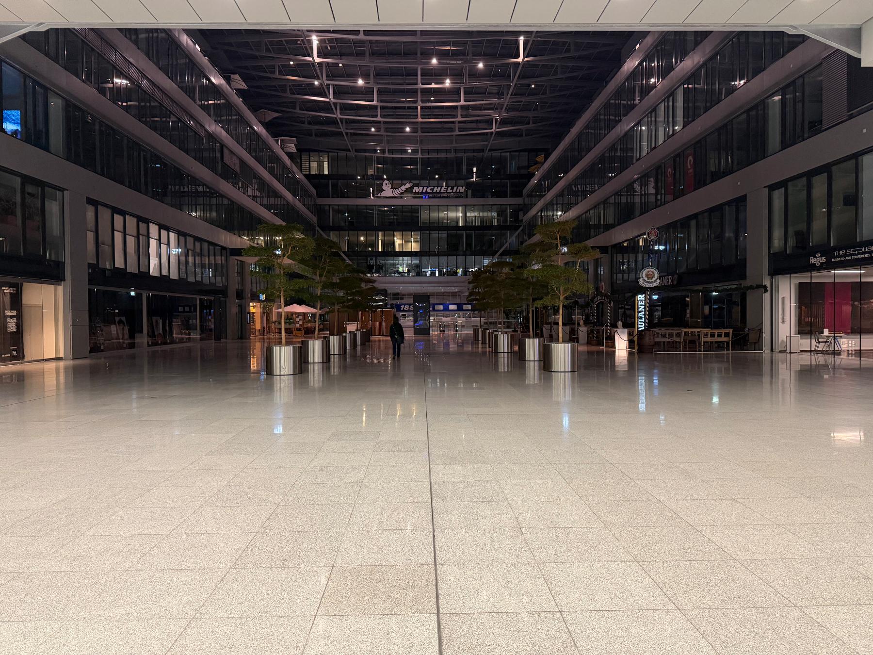 Looking between an indoor lit up area of the Squaire into a darkened area. There’s the back of a lone person in the distance