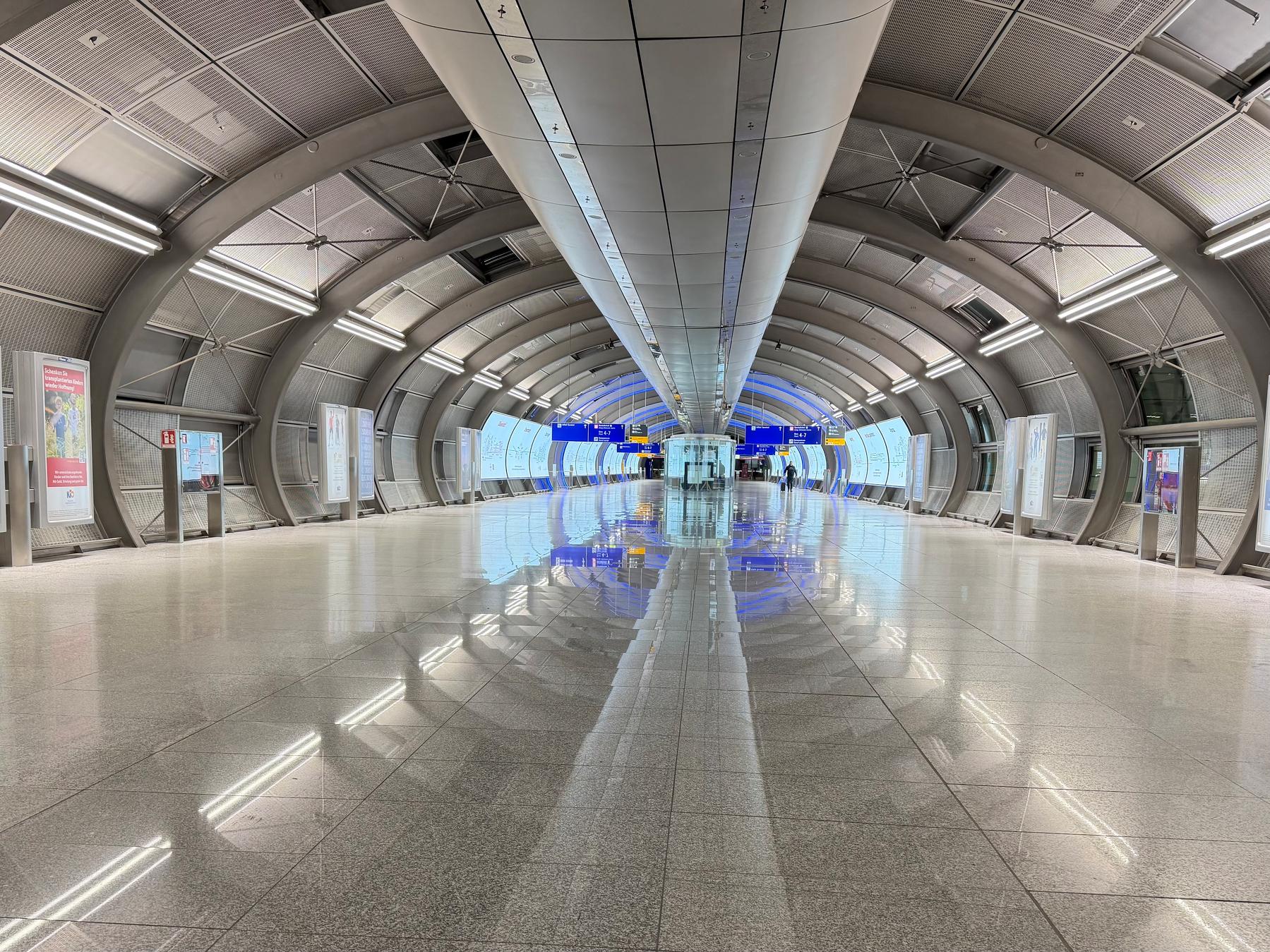 A wide oval walkway between Frankfurt Airport and the train station at the Squaire. The floors reflect thr ceiling lights giving the hall a futuristic kind of look