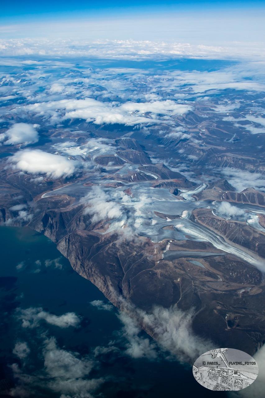 Top down View on a Fjord with mountains and valley with ice and clouds further back.