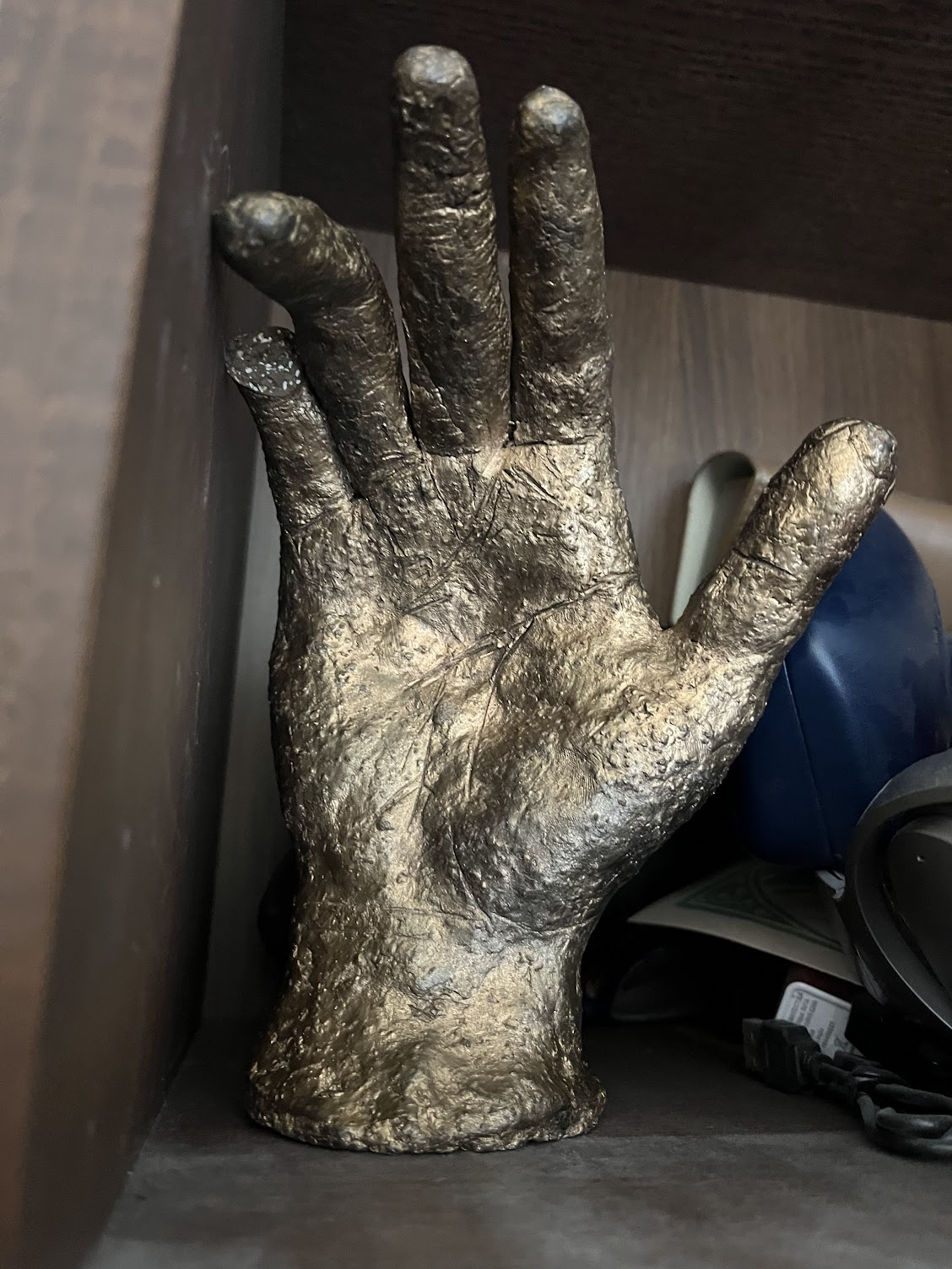 On a cluttered shelf, a stone hand painted a chunky gold. It's missing the tip of its pinky.
