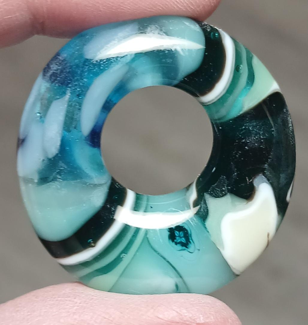 teal, aqua, black and white pendant with what appears to be banding diagonally positioned across the hole