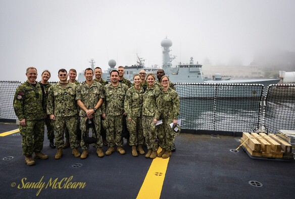 Combined US/Can medical team posing on deck with Danish ship in foggy background. 