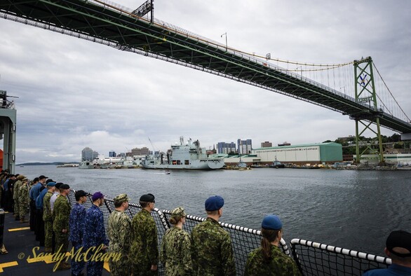 Crew lining the rail as ship passes under harbour suspension bridge during departure. 