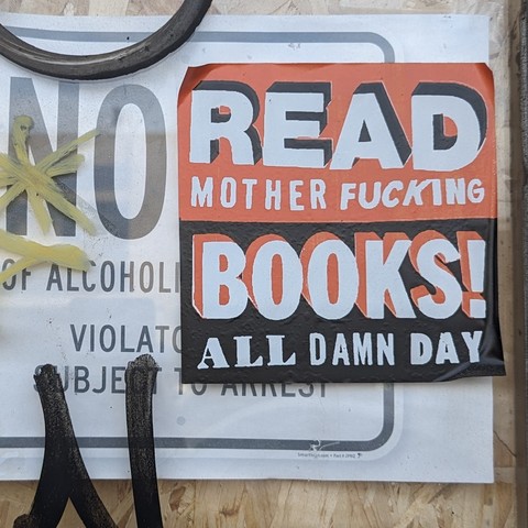 A red and black sticker

READ
mother fucking
BOOKS! 
_all_ damn day

Behind it is a sticker saying 
NO
...of alcohol
Violato[obscured]