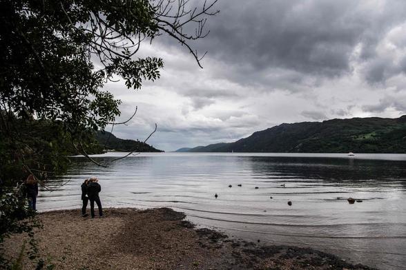 An image of a Scottish Loch with moody clouds, and two people standing on the shoreline.