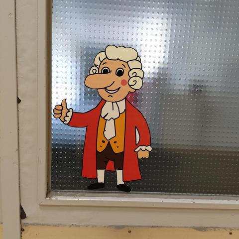 foto eines aufklebers einer gezeichneten comic-version von johann conrad schlaun mit perücke und historischer bekleidung, aufgeklebt auf eine tür mit glasscheibe
