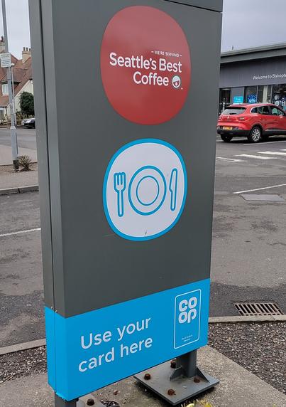 Part of the pillar sign at the entrance to a supermarket car park in Scotland. There's a logo for "Seattle's Best Coffee", and "Use your card here" and Coop logo