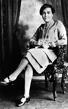 Fauset, seated, wearing a dress and a pearl necklace, looking directly at the camera.