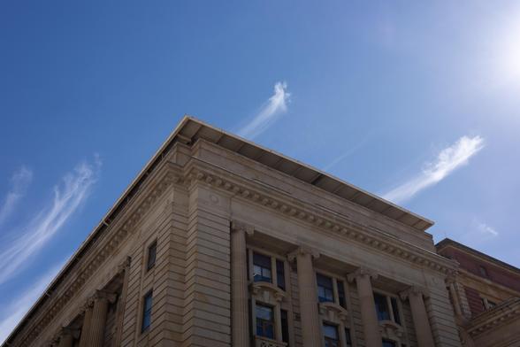 A corner view of a classical-style building with columns and ornate architectural details against a clear blue sky with wispy clouds.