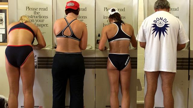 A row of men and women, backs to the camera, are seen wearing swimming attire while voting, metres from the Bondi surf. Credit: David Gray/REUTERS