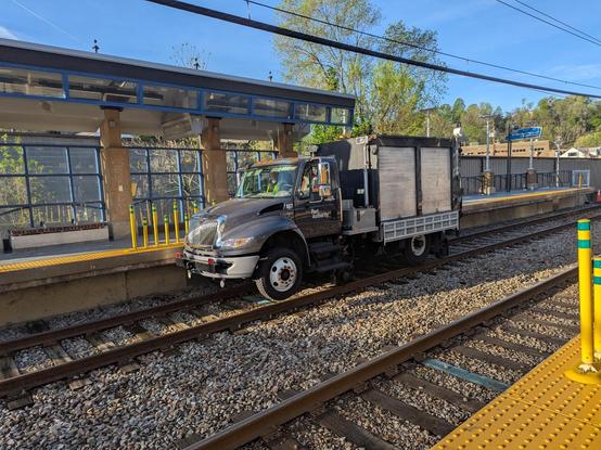 A truck on train tracks. The wheels with tyres are not on the tracks but another set of small metal wheels are