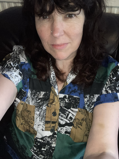 A middle aged woman with long hair wearing a 50s style shirt with colour blocks of green, blue, taupe, black and white