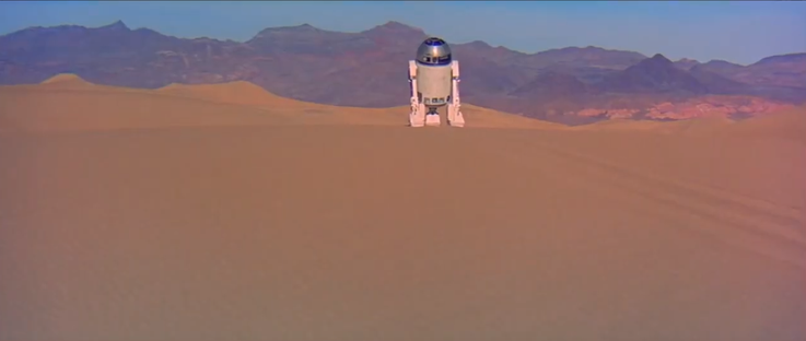 Droid wandering around on a sand dune, mountains in the background