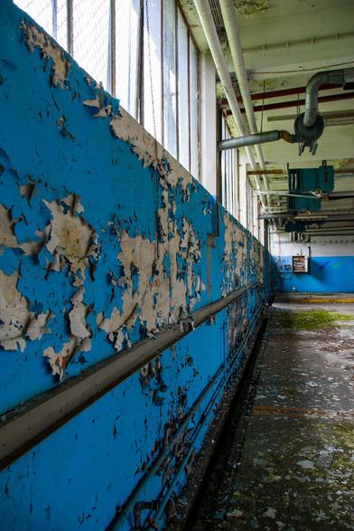 inside of an abandoned industry building. the blue paint is falling off the wall.