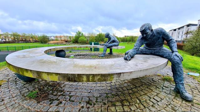 A sculpture of two men sitting at either end of an almost circular bench, writing on it.