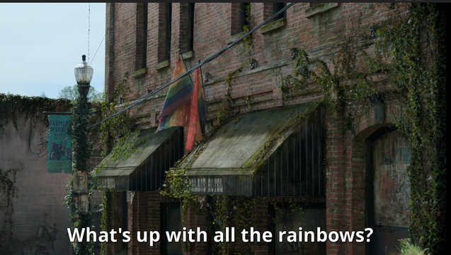 Une façade complètement délabrée avec de vieux drapeaux pride élimés qui pendent depuis le 1er étage (d'un immeuble - extrait de la série The Last of Us S02e4)