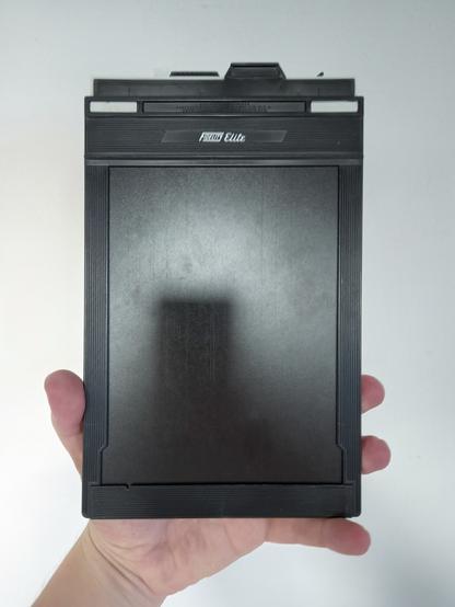 A hand holding a large 5x7" sheet film holder, aka a double dark slide (or DDS)