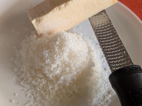 A mound of freshly grated Parmesan next to a thin rectangular block about 1"x1"x 6" leaning on a microplane grater all on a plate