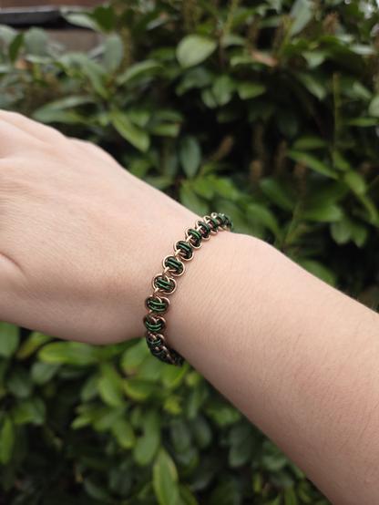 A chainmaille bracelet in the barrel weave style, in bronze and green, worn on my wrist
