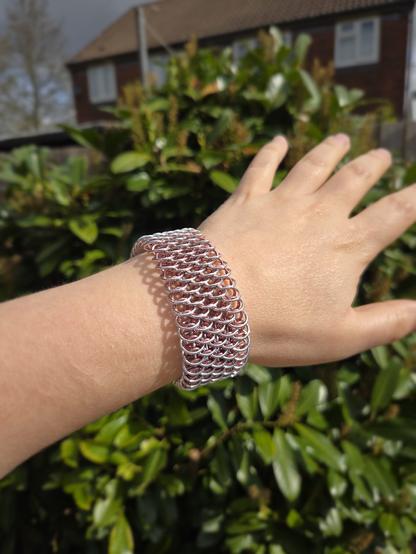 A chainmaille bracelet in dragon scale weave, made of pink and silver rings, worn on my wrist