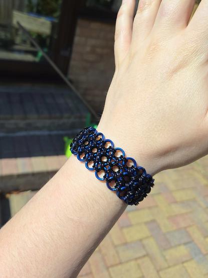 A chainmaille bracelet in Japanese weave, made of black and blue rings, worn on my wrist