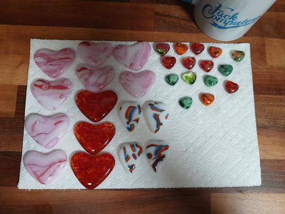 the hearts are laid out on a paper towel. there's white ones with rainbow streaks, pink ones and fiery ones, plus a bunch of miscellaneous ones. also my mug says fuck computers. it's sitting next to them
