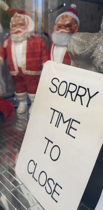 Sign saying “SORRY TIME TO CLOSE” with two vintage Father Christmas figurines behind it that look slightly creepy.