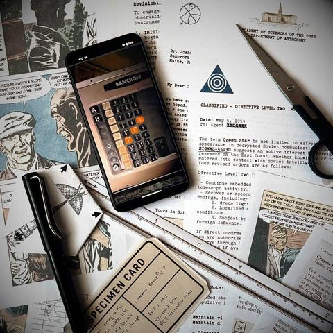 A top-down photograph of the printed materials for the game 'The Green Star' scattered on a desk. In the center, a smartphone displays a 3D retro-style telescope control panel with orange glowing buttons. Surrounding the phone are 1950s-style documents, a specimen card and a folded origami model of a fly.