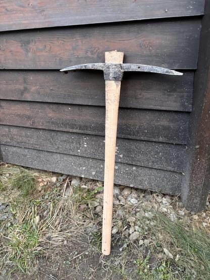 A large pickaxe leaning against the outer wall of a house