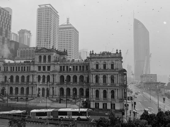 Black and white shot out a rainy window. Old style building and busses.
