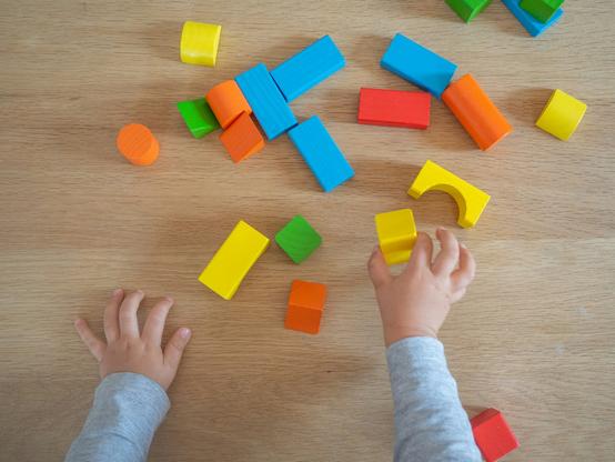 A photograph of the arms and hands of a child playing with colourful blocks