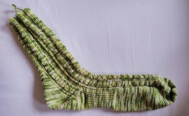 A hand-knit sock on a white background. 

The sock is made from green white variegated yarn. Pattern is textured with cables.