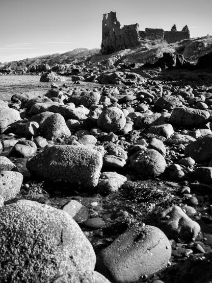 The stone ruins of Dunure Castle standing proud on the skyline overlooking the Firth of Clyde, while at low tide the water has receded over the large boulders which line the shoreline in the foreground