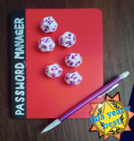A red notebook on a wood surface. The notebook has white writing along the spine that reads, "password manager" in white block letters. A handful of polyhedral dice with pairs of alphanumeric characters on each side have been spread across the notebook. A purple mechanical pencil lays diagonally across the notebook. In the corner of the image an advertisement-like award-shaped badge reads, "this year's best."