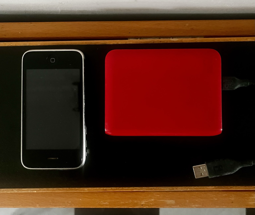an upside down iphone4 sits next to a small, red external hard drive, probably swapping stories about their various health issues & recuperations.