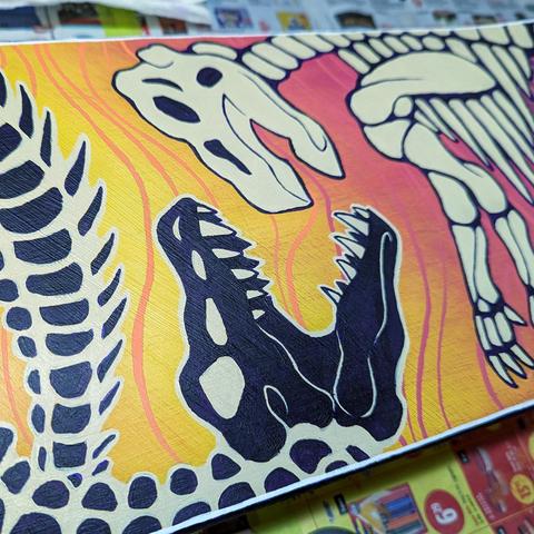 A close up of a painted skateboard, showing two dinosaur skeletons facing each other.