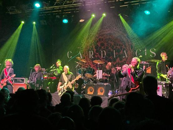 Cardiacs playing live at the QMU Glasgow on 13 March 2026. The bad is arrayed along a wide stage lit by green spotlights. The backdrop on stage is the (new) Cardiacs logo. 

From left to right:

Kavus Torabi, guitar and vocals; Chloe Herrington, saxophone and vocals; Rhodri Marsden, keyboards and vocals; Jim Smith, bass guitar and vocals; Bob Leith, drums; Sharron Fortnam, vocals; Mike Vennart, guitar and vocals; Craig Fortnam, percussion. 

(Photo by my friend Matt)