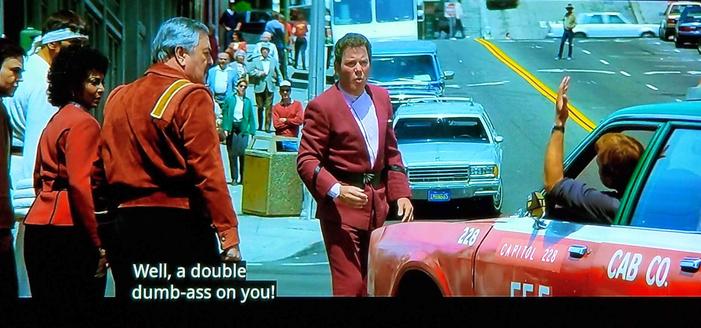 Star Trek IV the One with the Whales scene. We're on the streets of San Francisco in the 80s. Scotty, Uhura, Chekov, and Spock are on the sidewalk. Kirk is standing in the street arguing with the driver of a car who looks like he had to stop because Kirk got in his way. Car guy has his arm up & out the window in the air giving the international sign for "WTF are you doing!?" Kurt, conversely, has that "AYYYY, IM WALKIN' HERE" kind of face. (Also Spock is in a bathrobe)
Closed caption reads, "Well, a double dumb-ass on you!"