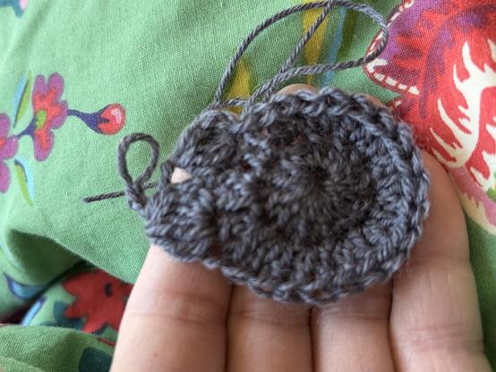 A grey blob of crochet. It is in the round 3rd row where I have started making bobbles. The back ground is a green fabric with flowery print.