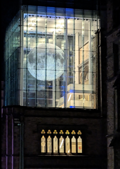 A very large model of the moon suspended high up in the ceiling at the Museum of Nature, seen from the outside through the windows.