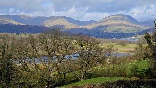 A spring view across fields and lakes towards distant mountains.