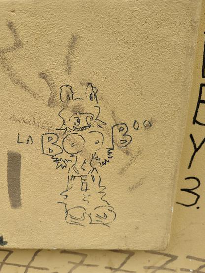 laBOOBoo, a... well endowed labubu showing its big... pun. drawn crudely on a wall.