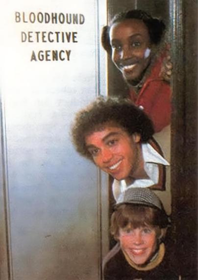 Three smiling kids peek out from behind a doorway beside a frosted glass panel labeled Bloodhound Detective Agency. The child at the top wears a red jacket, the middle child has curly hair and a white collared shirt, and the child at the bottom wears a detective style cap. The image has a soft, slightly grainy vintage look.