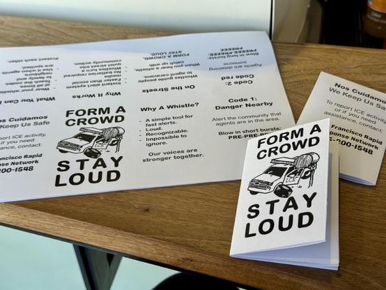 Stacks of paper with instructions on them. The zine is designed to be folded up into little booklets with instructions on what to do if ICE shows up. The front cover has an SUV that has been crushed by a giant whistle. Text says “form a crowd, stay loud”.